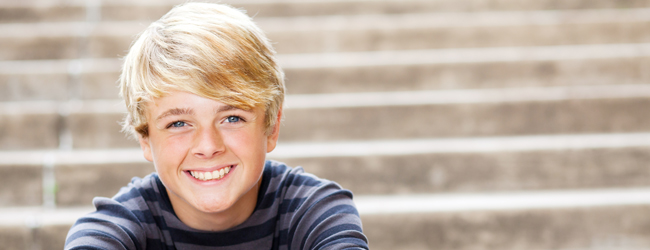 Ein blonder Junge mit blau gestreiftem Pullover lächelt